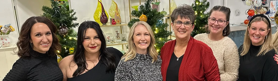 A group of people standing indoors in front of decorated Christmas trees and glass display shelves.